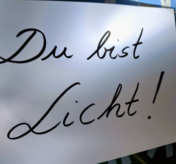 Ein weißes Schild, das von oben angestrahlt wird und auf dem steht: Du bist Licht!