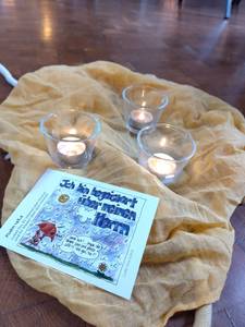 Ein hellorangenes  Tuch liegt auf dem Boden, darauf stehen 3 brennende Teelichter im Glas, auf einer Karte neben den Teelichtern steht: Ich bin begeistert über meinen Herrn